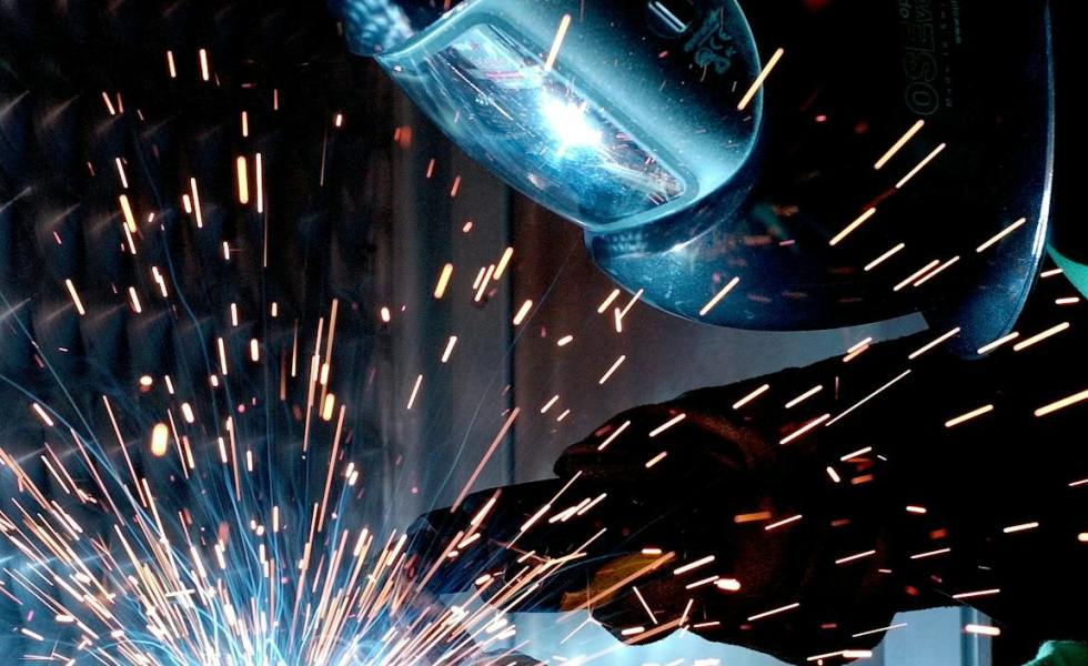 person in welding mask while welding a metal bar